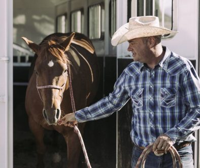 A man taking his horse out of a horse trailer.