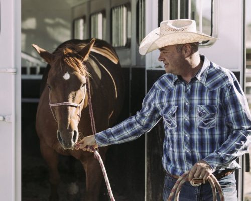 A man taking his horse out of a horse trailer.