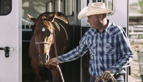 A man taking his horse out of a horse trailer.