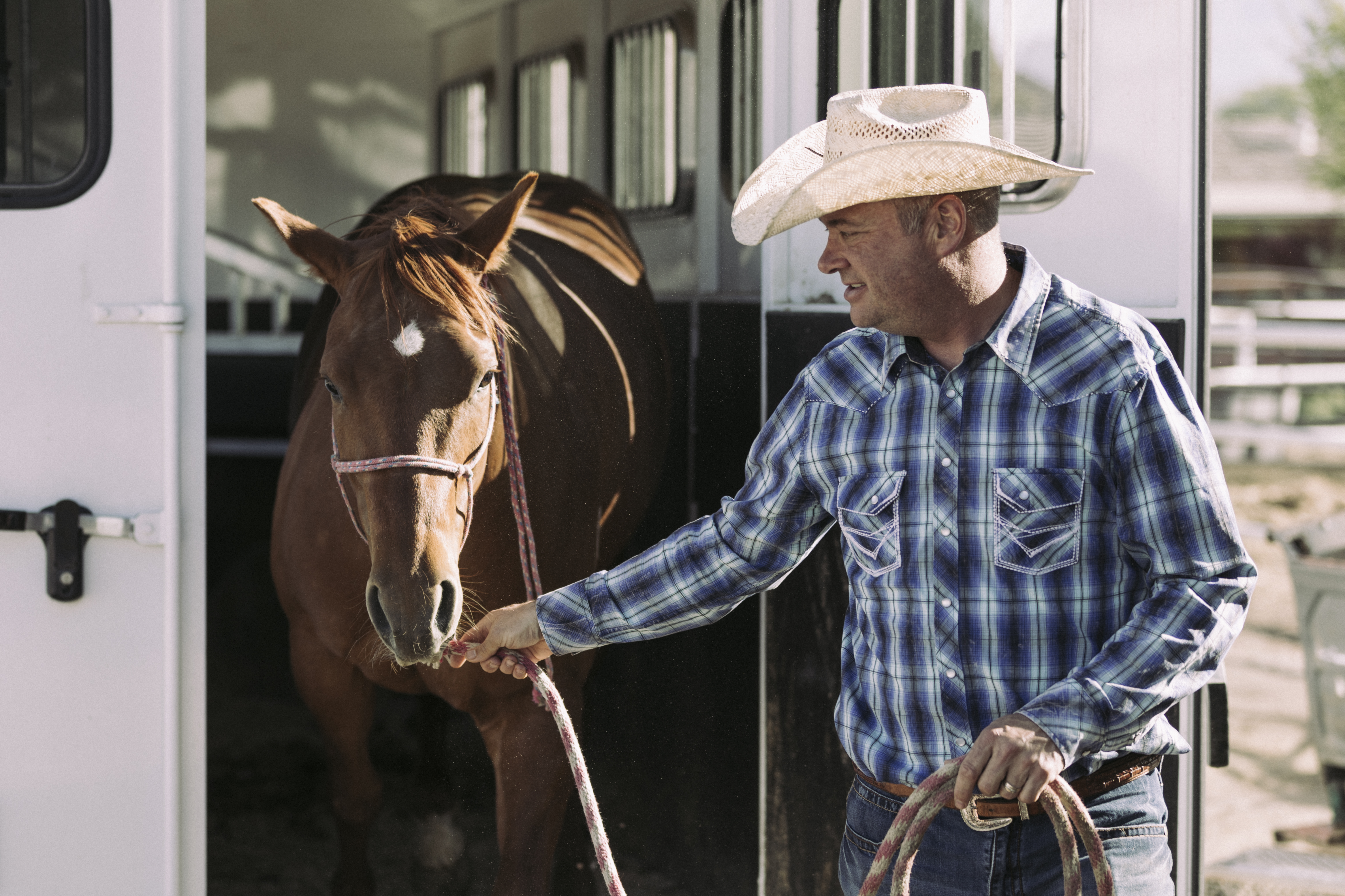 A man taking his horse out of a horse trailer.